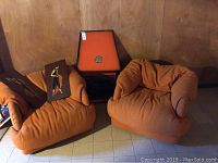 Overall view of two orange chairs, electric fireplace console and two art panels