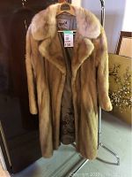 Full view of the beige-brown mink fur coat hanging on a rack, showing its knee-length and dense fur texture.