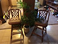 Two wicker swivel bar stools with attached fabric cushions next to a white wooden planter with green plant.