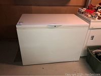 White chest deep freezer in basement, closed, showing overall condition and placement.