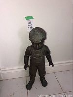 Front view of little boy statue standing upright against white wall, showing full body and posture.