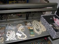 Overview of costume jewelry including pearl-style necklace, white bead necklaces and bracelets, and jewelry case.
