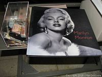 Top view of Marilyn Monroe book by Marie Clayton and a transparent box containing assorted collectible items including costume jewelry