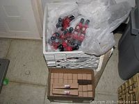Box and crate containing numerous bottles of Sally Hansen nail polish in red hues and darker tones, wrapped partially in plastic bags.