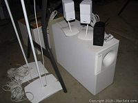 Two white speaker stands each holding two white cube Bose satellite speakers, one black cube satellite on top of subwoofer, white ported subwoofer on floor