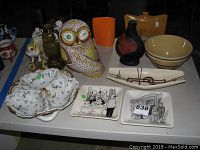 Table view of all items including ceramic owl figurines, various bowls, vases, and cartoon-themed plates