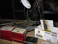Photo showing stacked vintage Regent cigarette boxes in red, smaller G.A. Georgopulo cigarette box, black desk lamp, and a few cable ties.