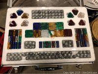 Top view of foam tray with colorful plastic rods, connectors, and metallic spheres arranged in compartments inside metal carrying case.