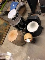 Wide shot of three drums and hexagonal storage seat on a concrete floor.