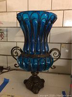 Front view of blue glass vase showing ribbed glass and metal wire frame with curled handles.