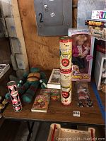 Photo of assortment of vintage toys on table including Teenage Mutant Ninja Turtles plush, kaleidoscopes stacked, boxed Mommy Doll, boxed Barbie doll, and vintage music book.