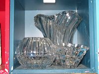 Three clear glass vases placed inside a blue shelf, showing round, tall wavy, and triangular shapes.