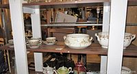 Shelving unit with various porcelain and china pieces including large decorative bowls and teacups with saucers.