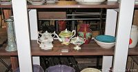 Wide view showing various German ceramics including a white floral sugar bowl, green and cream teapot, small floral pitcher, deep red vase, displayed on a shelf.