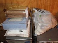 Stack of folded sheet sets and a plastic bag with towel, placed on top of metallic surface, wood background.