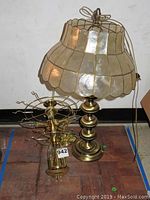 Brass table lamp with beige Capiz shell style shade and round brass base, about 27 inches high, placed near a brass hanging light fixture on floor.