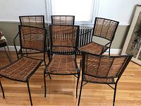 Front angled view of 6 chairs, 2 with arms (captain) and 4 armless chairs showing rattan seats and backs on black wrought iron frames