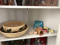 Two vintage ovenware bowls with floral designs, pottery molds, and assorted colorful tea bag holders arranged on a shelf.