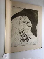 Framed black and white pencil sketch of a person with a large dark hat holding a flower, showing signature area and condition.