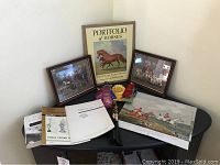 Photo showing Portfolio of Horses book, two framed horse prints, horse ribbons, horse-related books arranged on a table