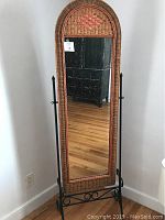 Full view of multicolor rattan framed full-length floor mirror with black metal stand, showing woven rattan texture and arched top.