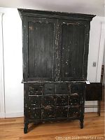Full front view of distressed black two-piece wood armoire showing top doors and 12 bottom drawers