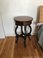 Full view of the round side table showing the black sculpted base and drawer under the top.