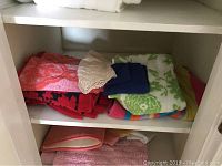 Shelving with various folded towels in coral, red, blue, green, and patterned colors. Includes lace trimmed white fabric and washcloths.