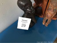 Close-up photo of a dark wood bust sculpture resembling an African theme figure and partial view of wooden carved items
