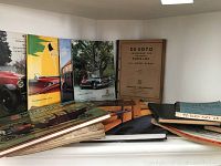 Wide view of vintage car reference books arranged on a shelf, including colorful book covers with classic cars and a DeSoto parts list.