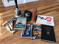 Overview of the lot showing books on historical and military subjects, the large silver-colored veterans bell, and the Air Force hat.