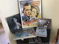 Framed Casablanca movie poster displayed upright alongside black and white Elizabeth Taylor photo, Beatles booklet, and other vintage photographs on a table