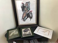 Photo showing large framed Audubon woodpecker print above, three smaller framed bird prints and one unframed signed bird print on a black table