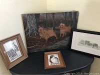 Four pieces of framed animal art displayed on a black table and floor corner: a dog oil painting, a pencil sketch of cats, and two drawings of birds (eagle, owl and chicken).