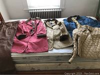Five jackets and one pair of pants laid out on a bed, showing a variety of colors and styles including barn and quilted jackets.
