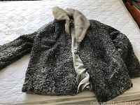 Full view of gray Persian lamb fur jacket laid out on bed showing curly textured fur and light-colored mink collar