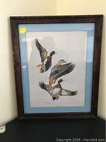 Full view of wood framed art print of three mallard ducks in flight with blue mat.