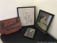 View of the framed artworks and sign displayed on a black surface against a white wall.