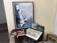 Full view of the framed Eric Clapton poster, vintage Bambi print, signed watercolor and two Haitian oil paintings on wooden boards.