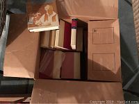 Box containing approximately 10 vintage hardcover Zane Grey books with protective tissue sleeves, showing variety of bindings and colors.