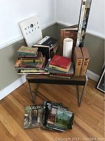 Corner setup showing a collection of stacked vintage books including 'Whole Earth' and larger brown hardcovers, as well as nearby Paris prints on the floor.