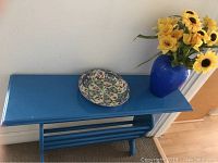 Front angle of blue painted table with ceramic divided dish and blue vase with yellow artificial sunflowers on top