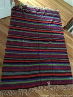 Full view of flat-woven striped rug laid on hardwood floor showing colorful horizontal stripes and white fringes on one end.