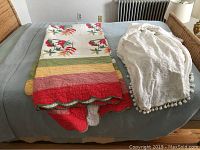 Photo of all three bedspreads displayed on a bed, showing the white pom pom bedspread and leaf theme quilt