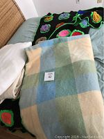 Photo showing both blankets laid on a bed, the LL Bean wool blanket with pastel colors and the Ralph Lauren colorful crochet blanket underneath