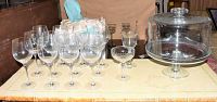 Clear and green crystal wine glasses displayed with glass domed cake plate on table.