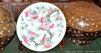 Two black lacquer bowls with lids flanking a white decorative plate with red fruit and green leafy motif