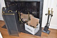 Wide shot showing both fireplace screens in front of fireplace and a box with small tools.