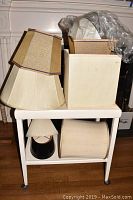 White rolling cart with multiple lamp shades stacked on top and stored below, showing full lot contents.
