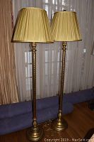 Two matching brass floor lamps standing side by side with pleated gold lampshades, showcasing full height and base design.